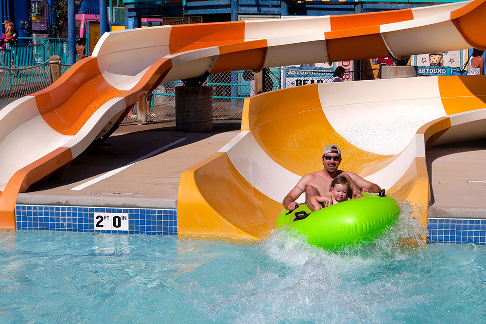 Father and little girl on sliding on water tube at big top, water world